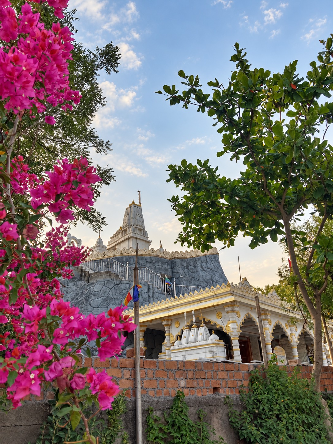 बोगनवेलिया और वृक्षों के बीच से दिखता शिला पर्वत, शिखर और नीचे का मंडप
