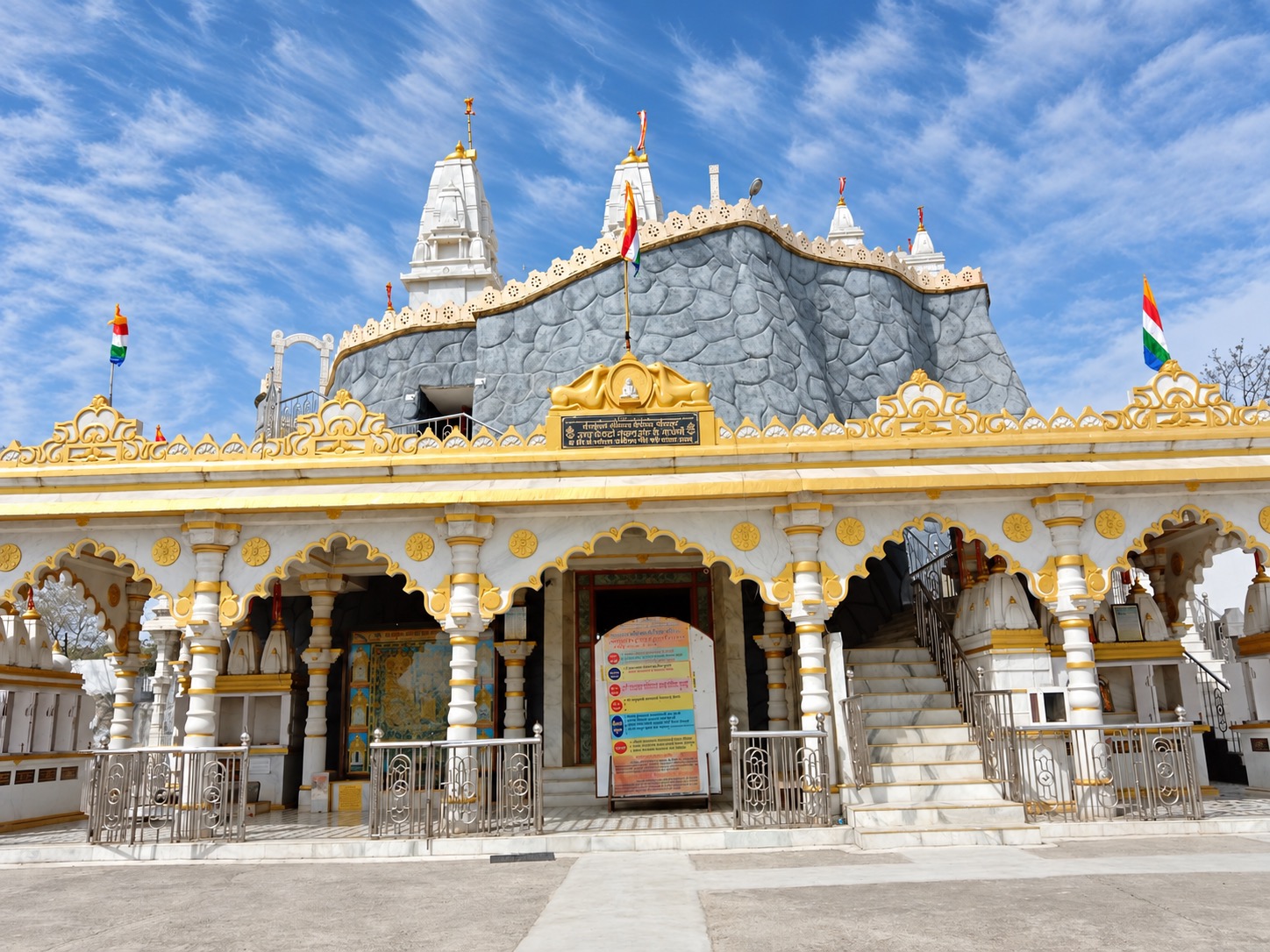दिन के प्रकाश में मंदिर का मुख — श्वेत-स्वर्णिम मेहराबें और ऊपर शिला पर्वत पर शिखर