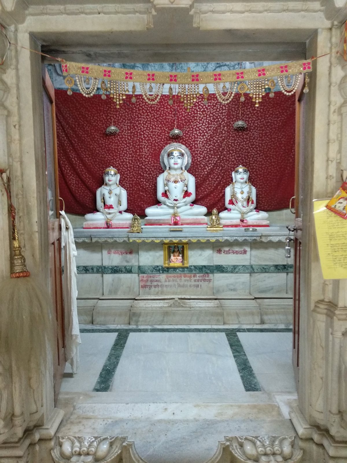 गर्भगृह में श्वेत संगमरमर की तीन तीर्थंकर प्रतिमाएँ, पीछे रक्तवर्ण पट